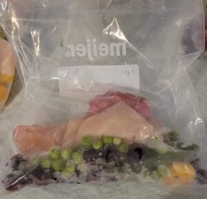 Sac allant au congélateur contenant de la viande blanche de poulet crue et des fruits.